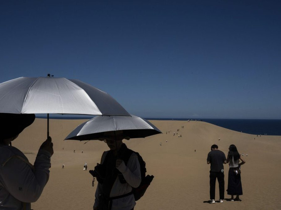 Turisti so slnečníkmi sa prechádzajú po piesočných dunách v Tottori.