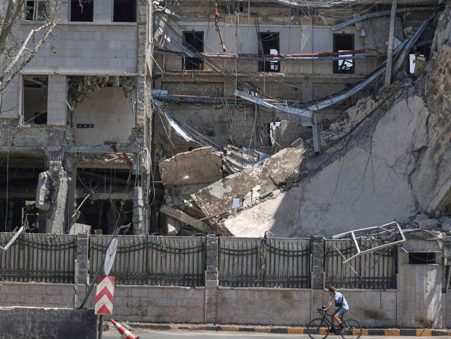 Na snímke muž prechádza na bicykli okolo zničenej budovy v Damasku.