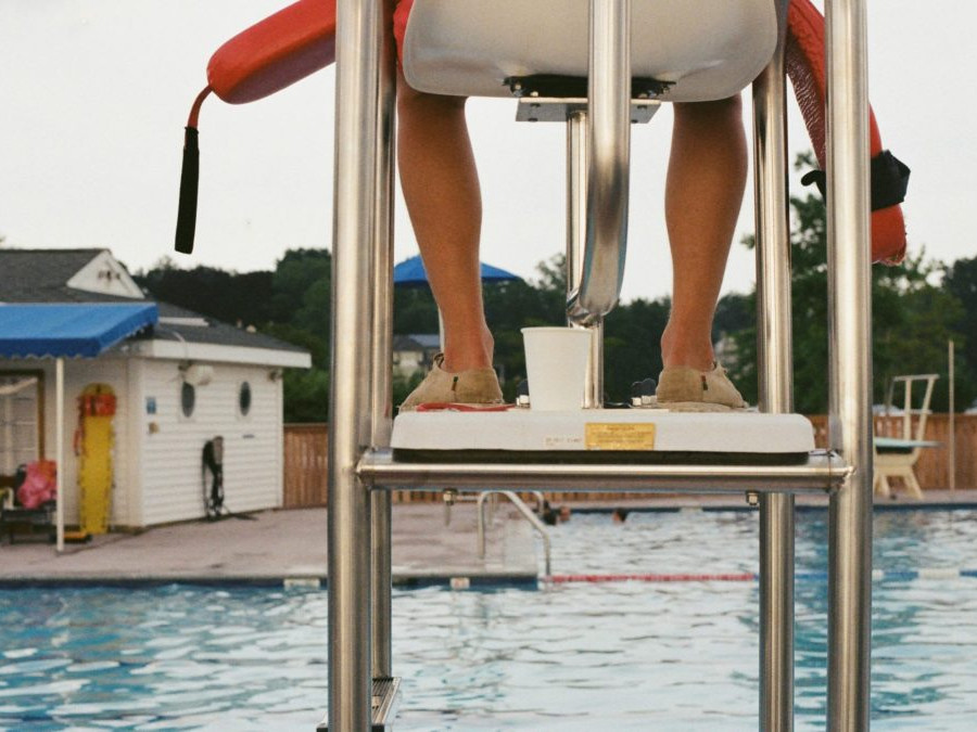 Plavčík sedí pri plaveckom bazéne.