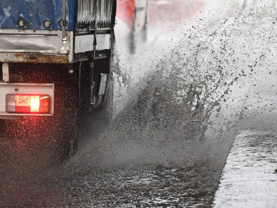 Ulica po búrke, prechádzajúce nákladné vozidlo z mláky špliecha veľa vody.