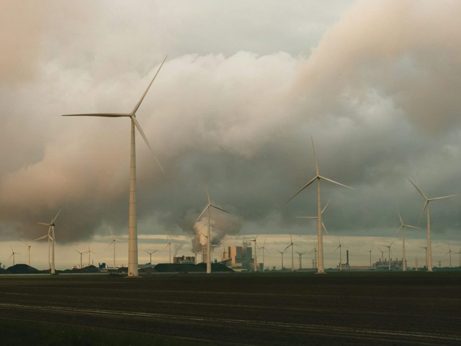 V popredí veterné turbíny, vzadu fabrika, z ktorej sa dymí.