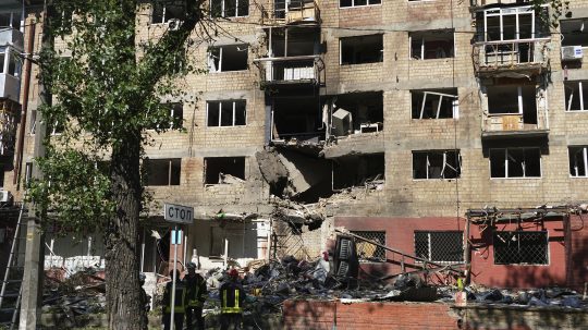 Zničená bytovka po úroku Ruska na Kyjev, pred ňou stoja hasiči.