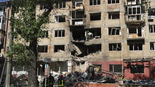 Zničená bytovka po úroku Ruska na Kyjev, pred ňou stoja hasiči.