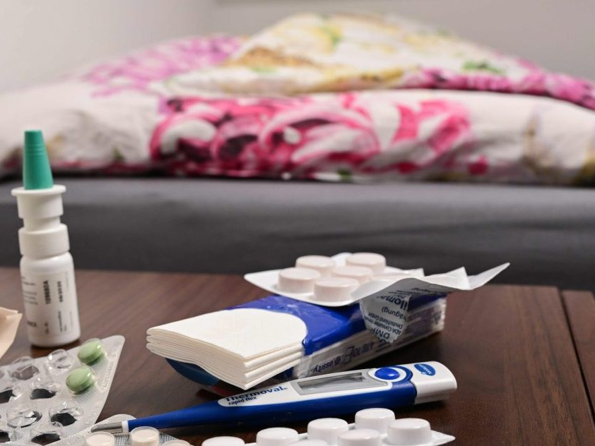 Tabletky a nosové kvapky na nočnom stolíku pri posteli.