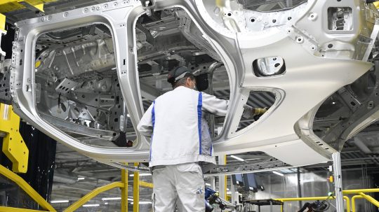 Pracovník v továrni Volkswagen pracuje s rámom vozidla.