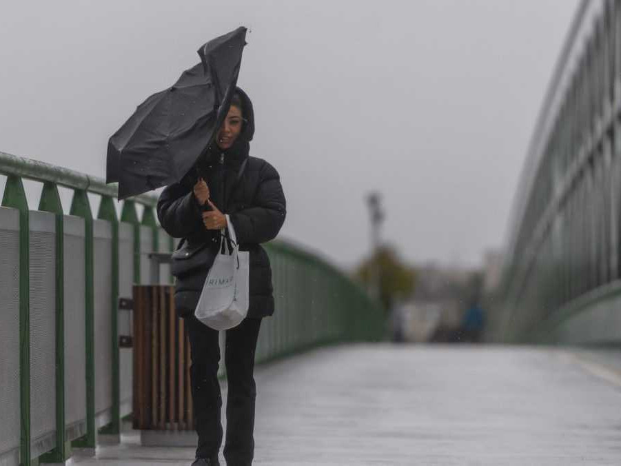 Žena s dáždnikom kráča počas vetra po Starom moste.