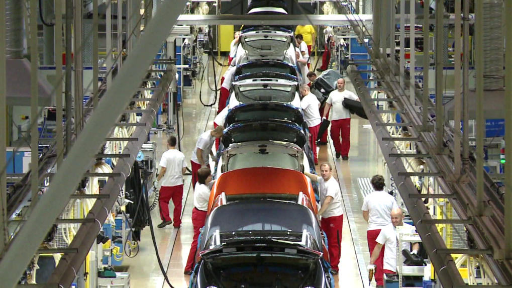 Vo fabrike na vozidlá muži pracujú za montážnym pásom.