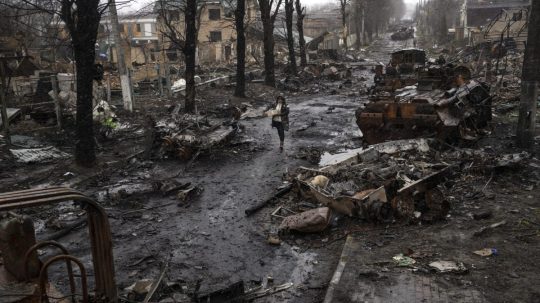 Žena kráča medzi zničenými ruskými tankami v ukrajinskom meste Buča.