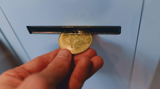 Osoba vhadzuje bitcoinovú mincu do priehradky v automate.