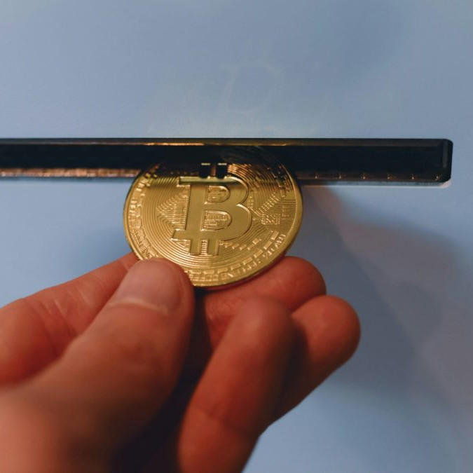 Osoba vhadzuje bitcoinovú mincu do priehradky v automate.