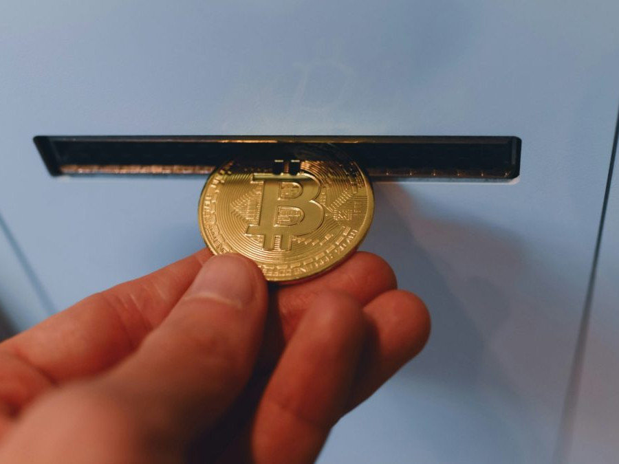 Osoba vhadzuje bitcoinovú mincu do priehradky v automate.