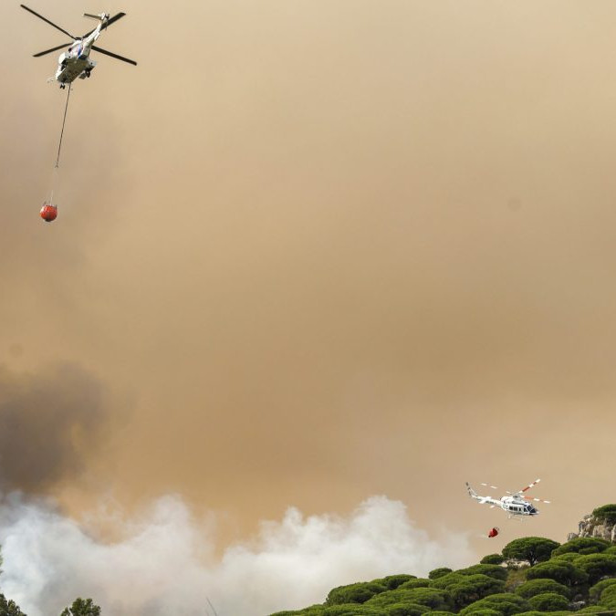 Na snímke je dvojica helikoptér, ktoré zhadzujú vodu na požiarom postihnuté lesy v Španielsku.
