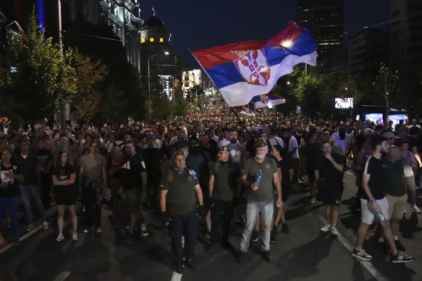 Demonštranti počas protivládnych protestov, nad nimi veľká vlajka Srbska.