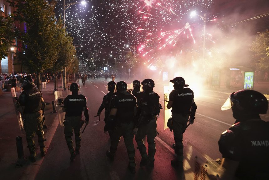 Demonštranti počas protivládnych protestov, v popredí policajti, pred nimi výbuch ohňostroja.