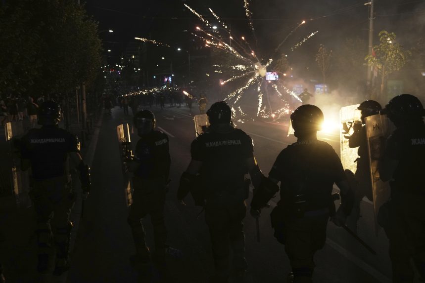 Demonštranti počas protivládnych protestov, v popredí policajti, pred nimi výbuch ohňostroja.