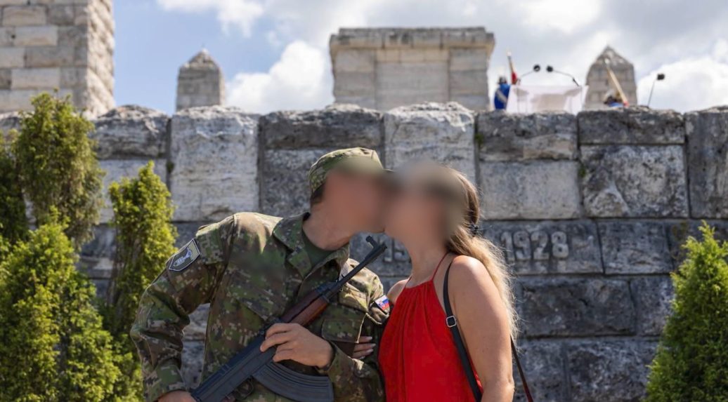 muž pózuje so zbraňou v ruke namierenou na ženu