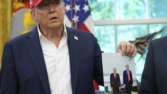 Na snímke Trump drží v ruke fotografiu zo stretnutia s Putinom.