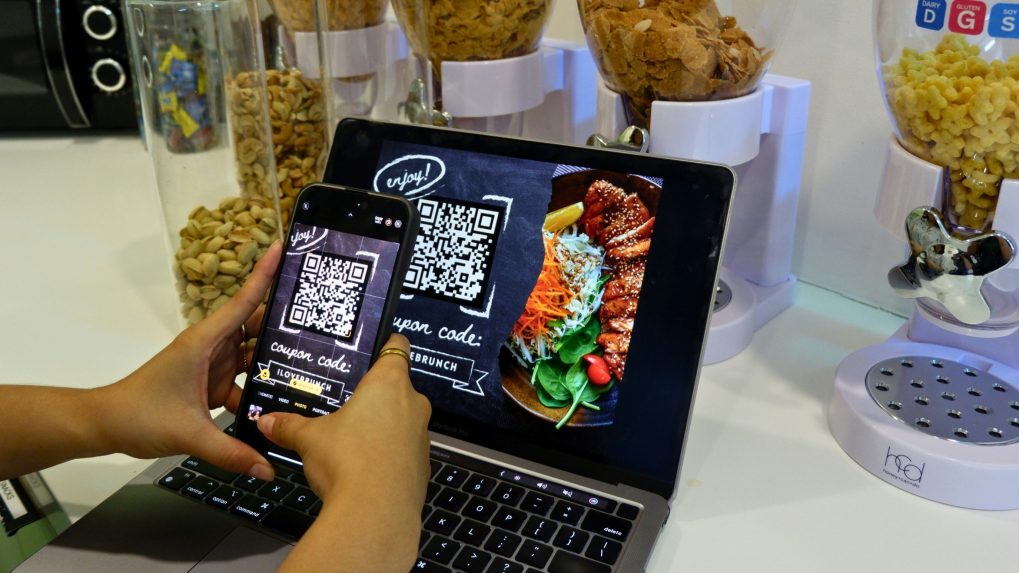 Na snímke osoba sníma fotoaparátom telefónu QR kód z obrazovky.