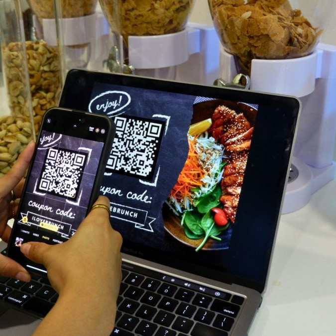 Na snímke osoba sníma fotoaparátom telefónu QR kód z obrazovky.