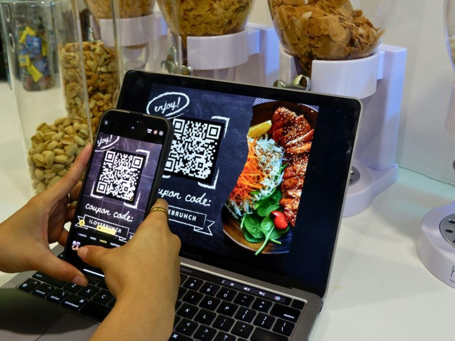 Na snímke osoba sníma fotoaparátom telefónu QR kód z obrazovky.