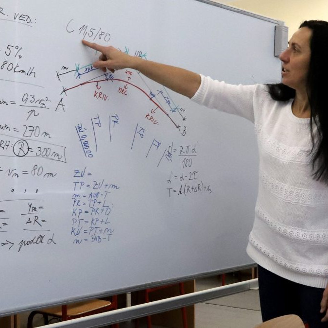 Na snímke je učiteľka, ktorá na tabuli vysvetľuje učivo z matematiky.