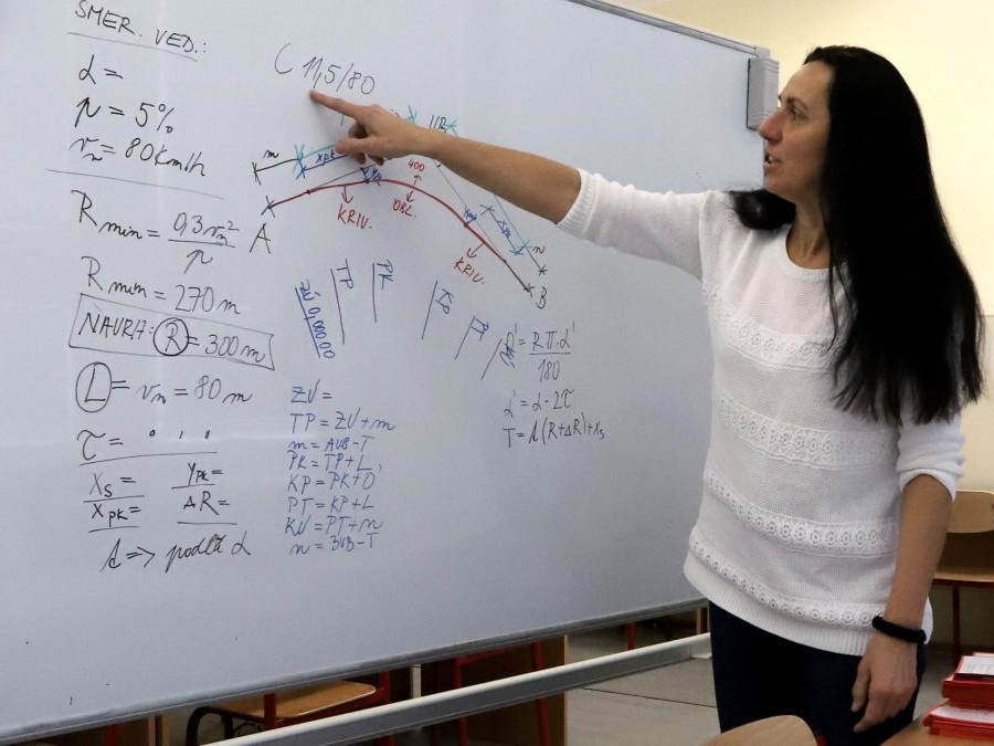 Na snímke je učiteľka, ktorá na tabuli vysvetľuje učivo z matematiky.