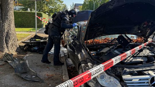 Policajt sa pozerá do vyhoretého auta v Mníchove, v popredí je policajná páska.