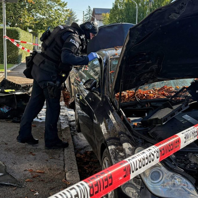 Policajt sa pozerá do vyhoretého auta v Mníchove, v popredí je policajná páska.