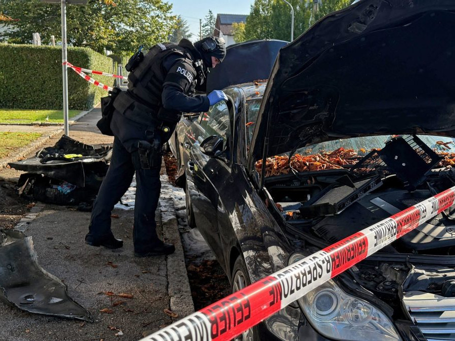 Policajt sa pozerá do vyhoretého auta v Mníchove, v popredí je policajná páska.