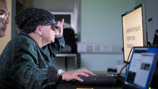 Pani Sheila so špeciálnymi okuliarmi pred monitorom počítača.