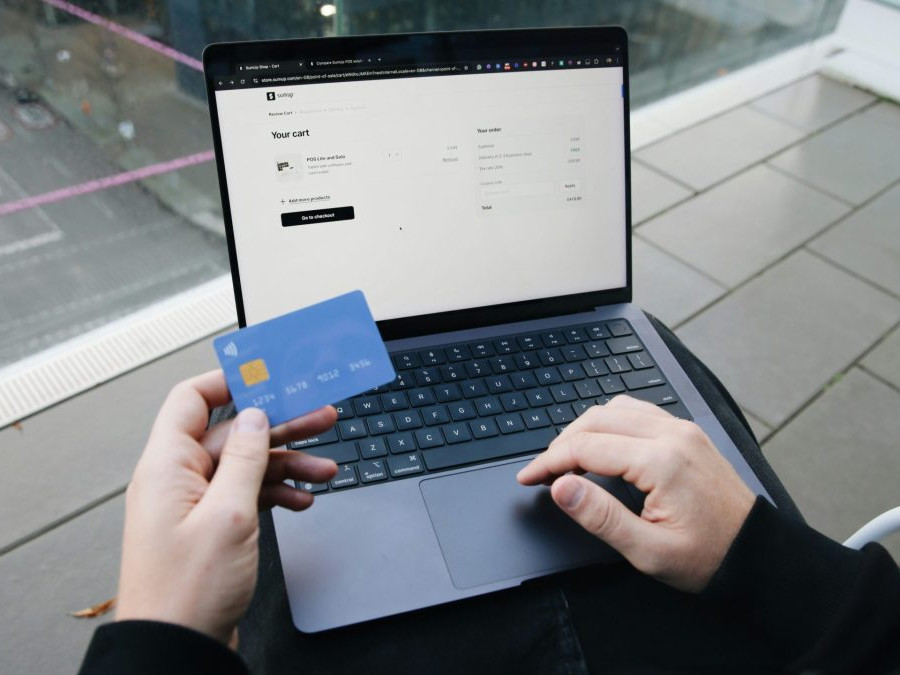 Na snímke osoba pri notebooku drží platobnú kartu.