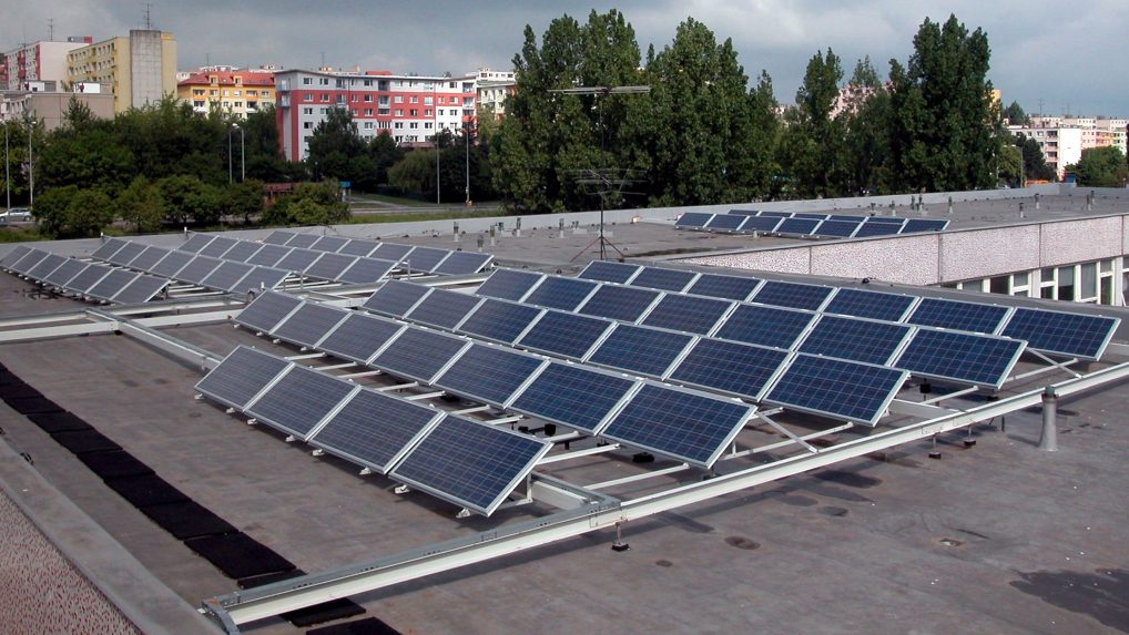 Na snímke solárne panely na plochej streche budovy, v pozadí paneláky.