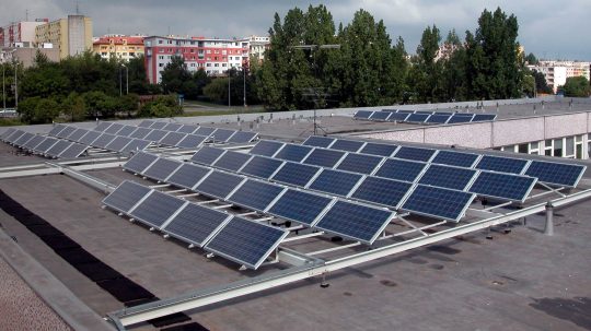 Na snímke solárne panely na plochej streche budovy, v pozadí paneláky.