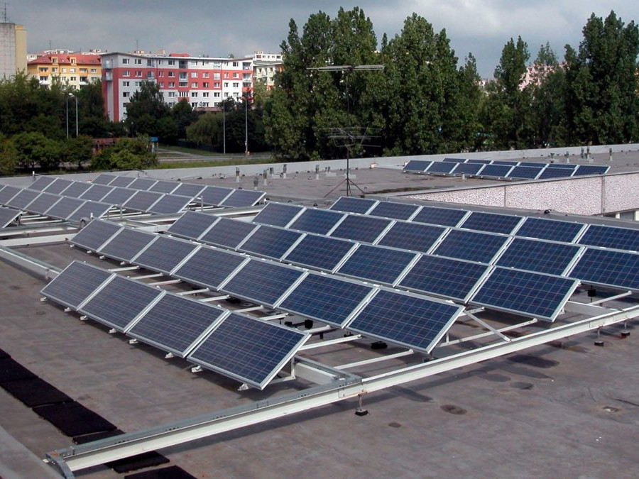 Na snímke solárne panely na plochej streche budovy, v pozadí paneláky.