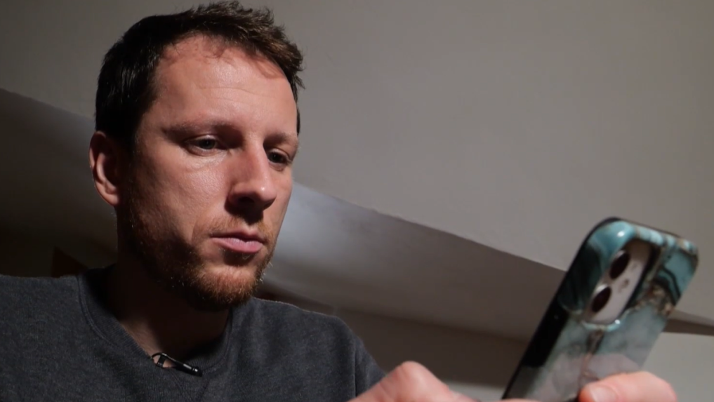 Na snímke muž, ktorého okradli podvodníci pozerá do telefónu.