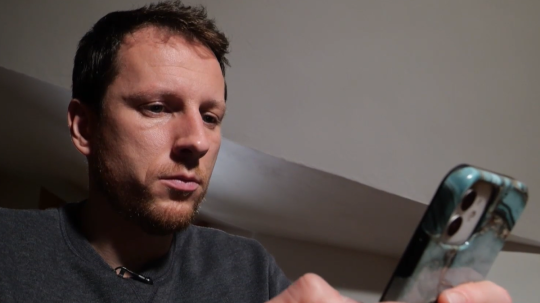 Na snímke muž, ktorého okradli podvodníci pozerá do telefónu.