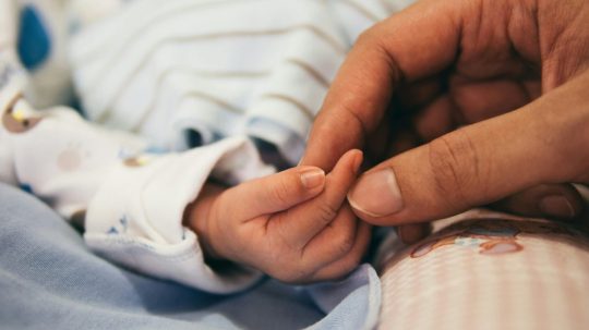 Na snímke ruka dieťaťa, ktorú drží ruka dospelej osoby.