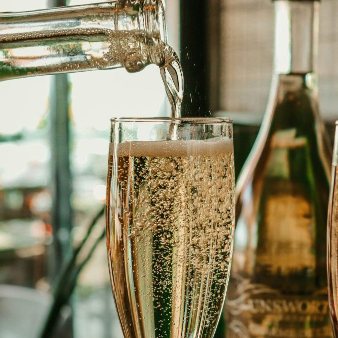 Z fľaše sa leje šumivý nápoj do úzkeho pohára.