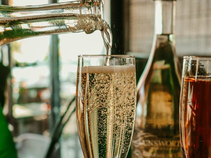 Z fľaše sa leje šumivý nápoj do úzkeho pohára.