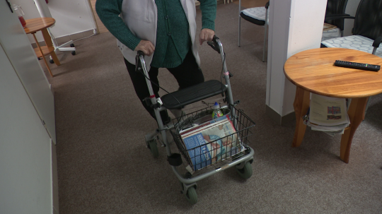 Na snímke je seniorka, ktorá sa opiera o vozík.