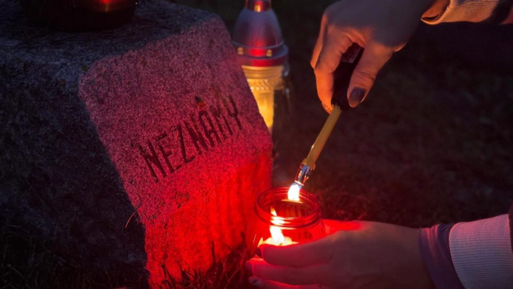 žena páli sviečku na hrobe