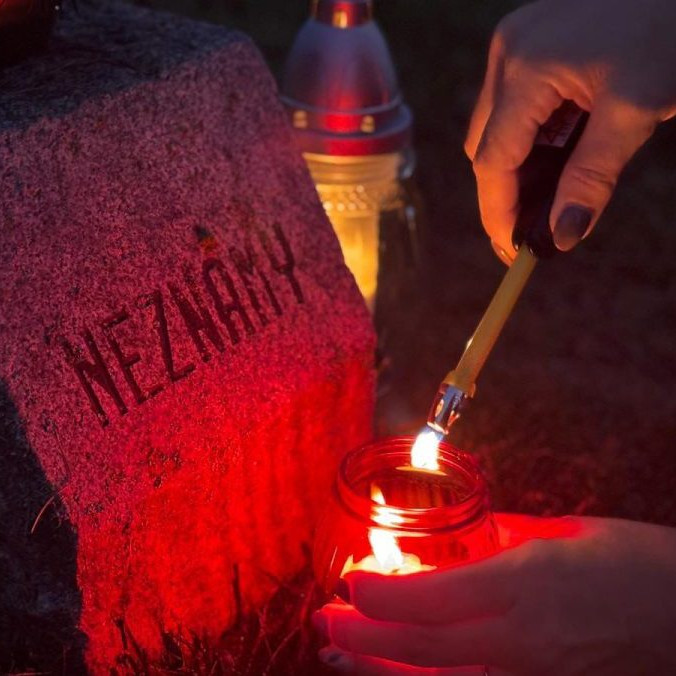 žena páli sviečku na hrobe