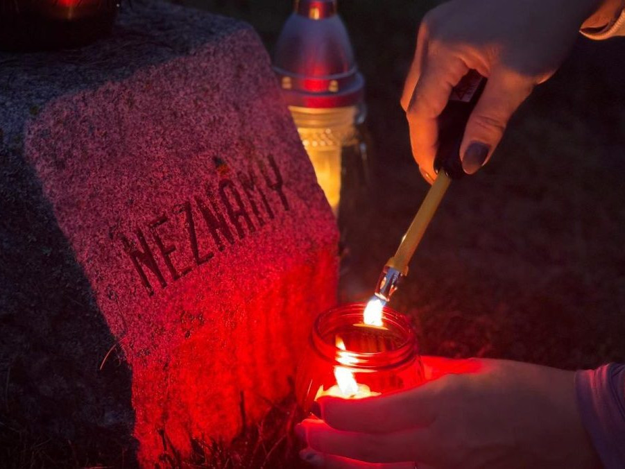 žena páli sviečku na hrobe