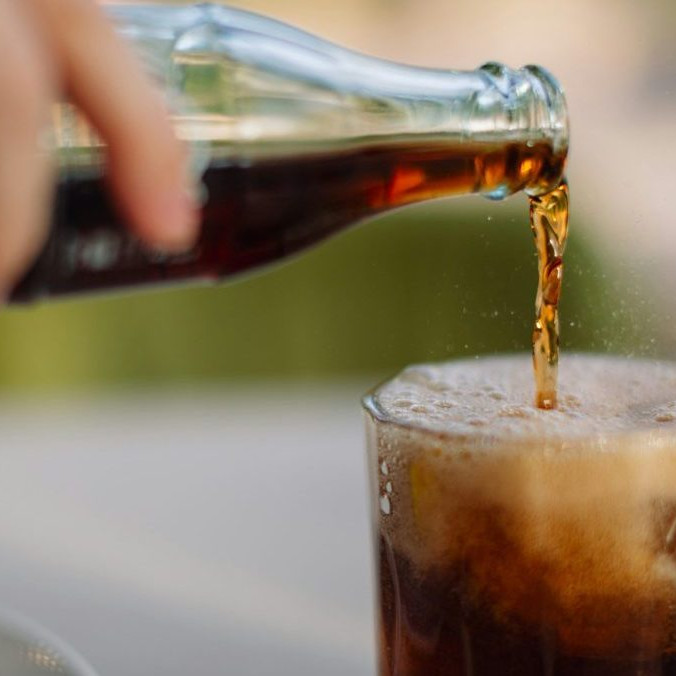 Na snímke osoba nalieva kolu z fľaše do pohára.