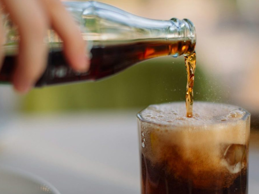 Na snímke osoba nalieva kolu z fľaše do pohára.