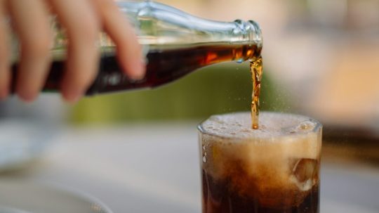 Na snímke osoba nalieva kolu z fľaše do pohára.