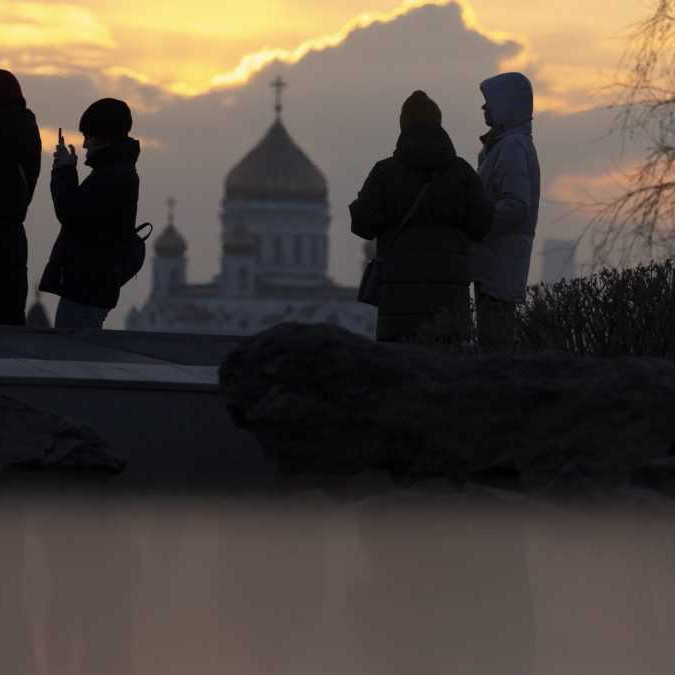 Ľudia sa prechádzajú počas západu slnka v parku Zaryadye s Chrámom svätého Vasila v pozadí v Moskve.
