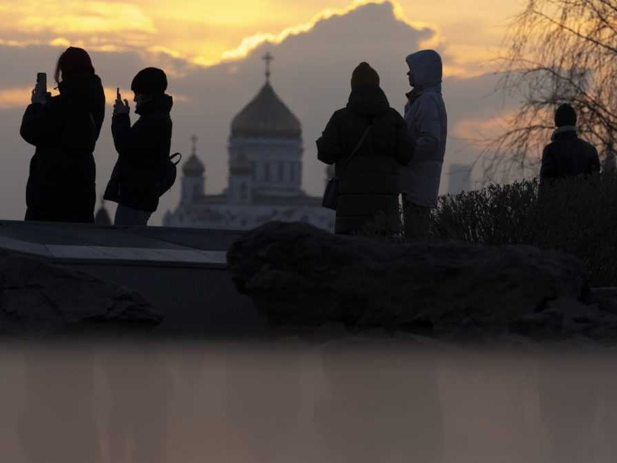 Ľudia sa prechádzajú počas západu slnka v parku Zaryadye s Chrámom svätého Vasila v pozadí v Moskve.