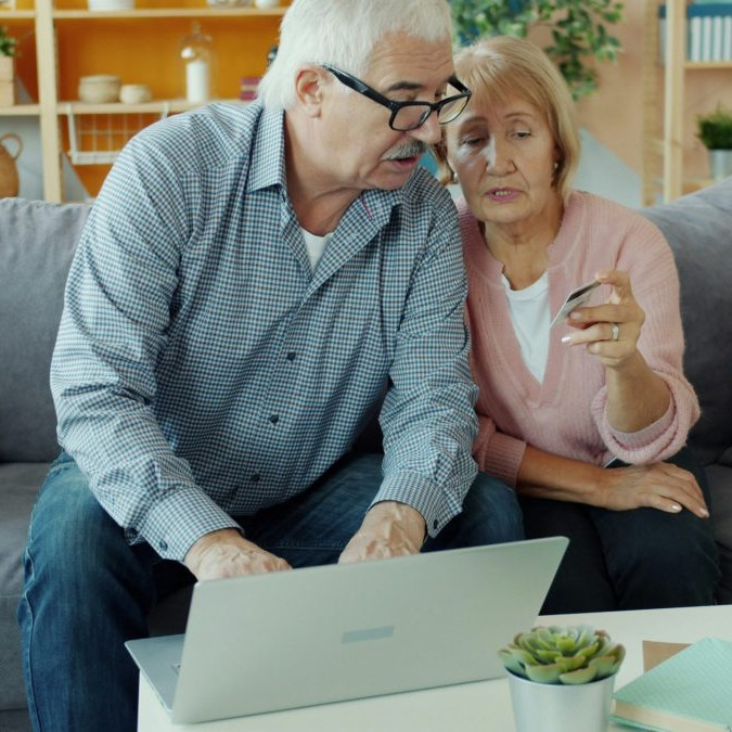 Na snímke je starší manželský pár, ktorý číta z platobnej karty údaje pre platbu na notebooku, ktorý majú pred sebou na stole.