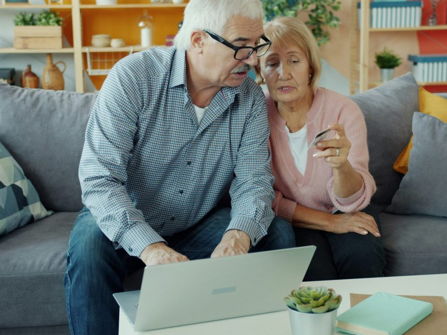 Na snímke je starší manželský pár, ktorý číta z platobnej karty údaje pre platbu na notebooku, ktorý majú pred sebou na stole.